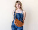 Woman wearing a blue striped dress with a brown leather bag against a plain background