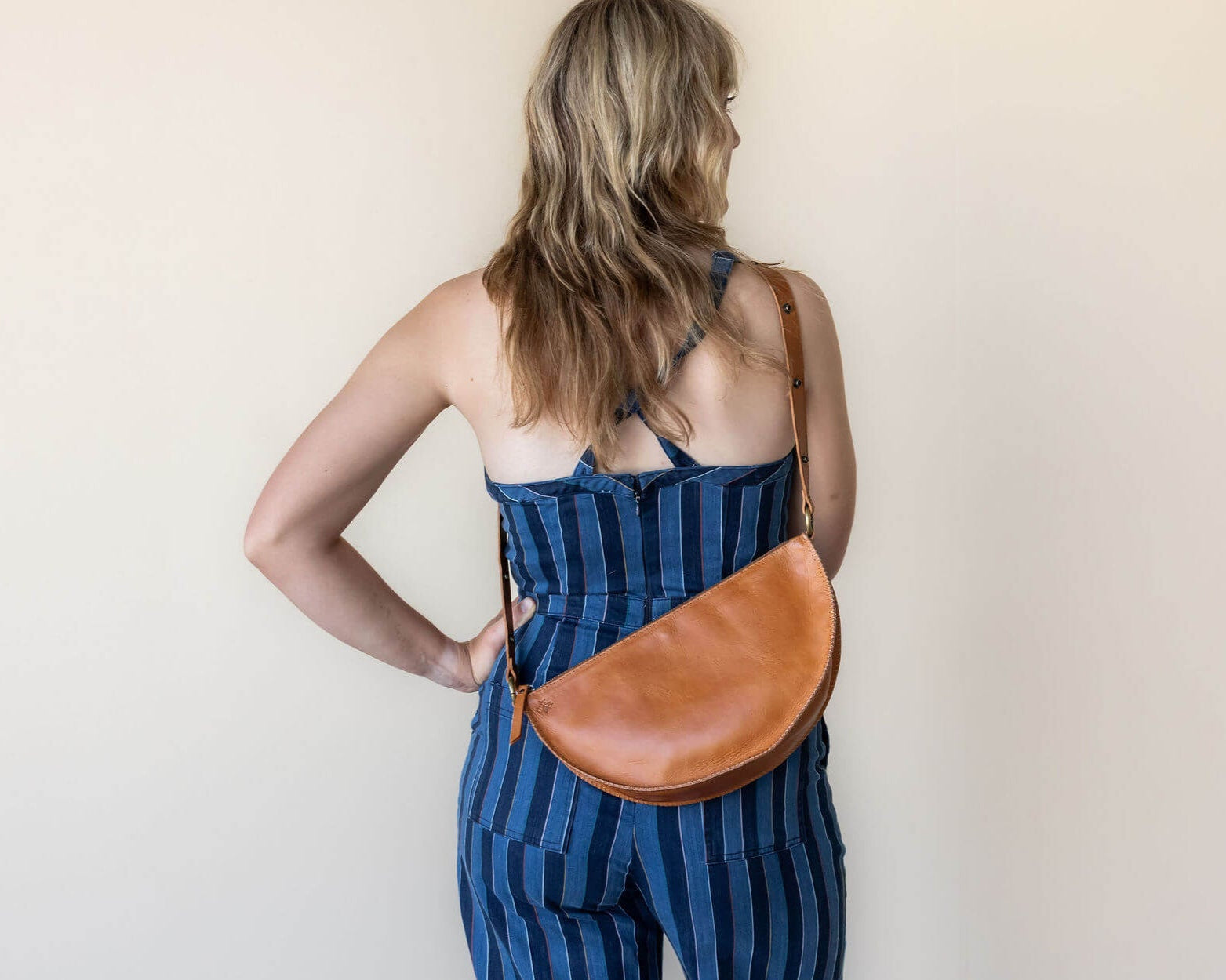 Woman wearing a blue striped dress with a brown leather bag on a plain background