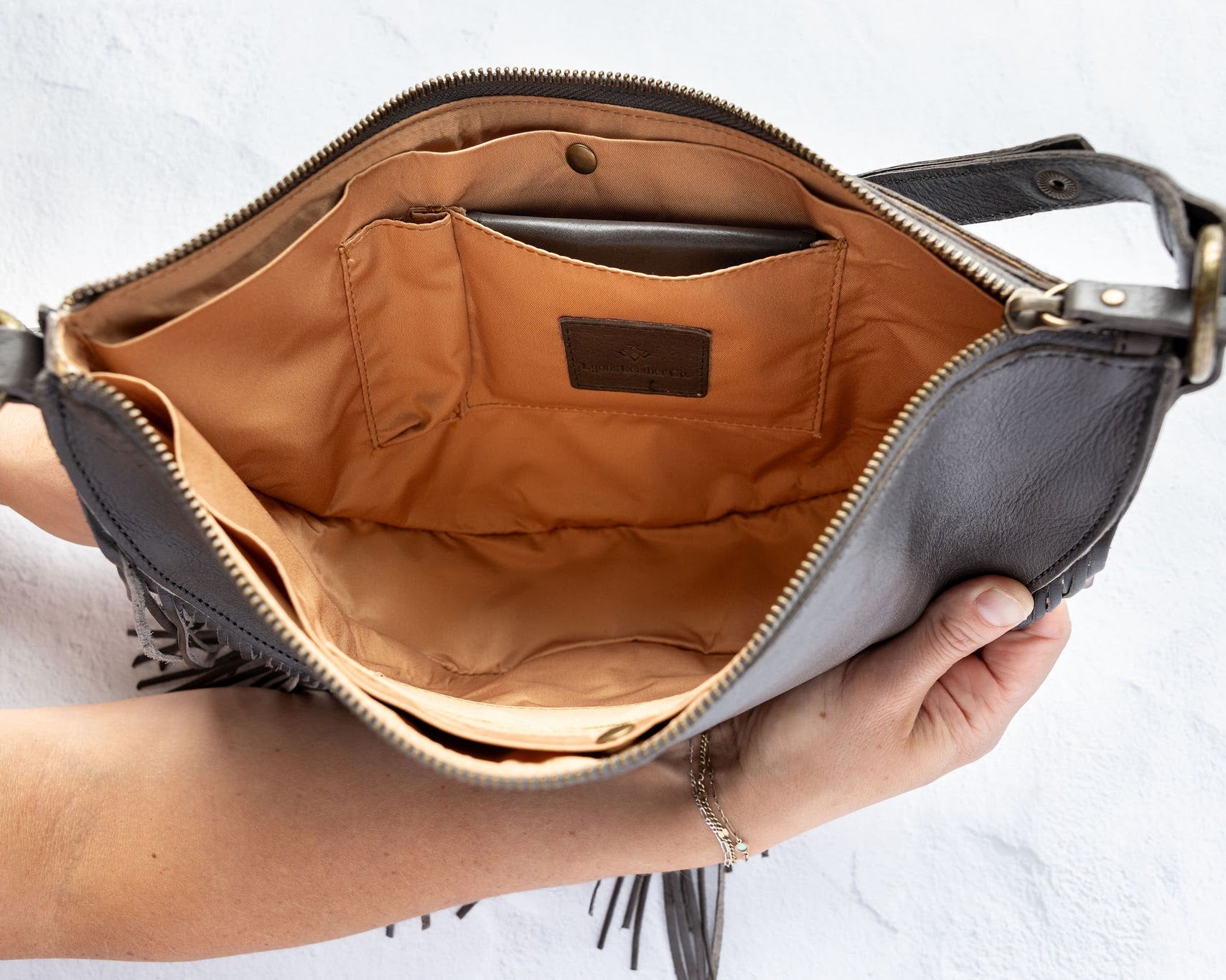 Charcoal leather fringe bag held open by a hand, showing the Gold lining, on a white background