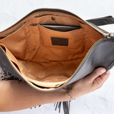 Charcoal leather fringe bag held open by a hand, showing the Gold lining, on a white background