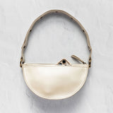 A small semi-circular cream leather shoulder bag with a matching leather strap and gold-tone hardware, displayed against a textured light gray background.
