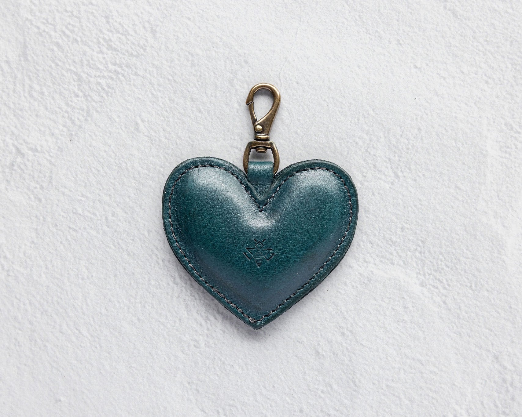 A heart-shaped teal leather bag charm with a brass lobster clasp