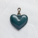 A heart-shaped teal leather bag charm with a brass lobster clasp