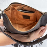 Charcoal leather fringe bag held open by a hand, showing the Gold lining, on a white background