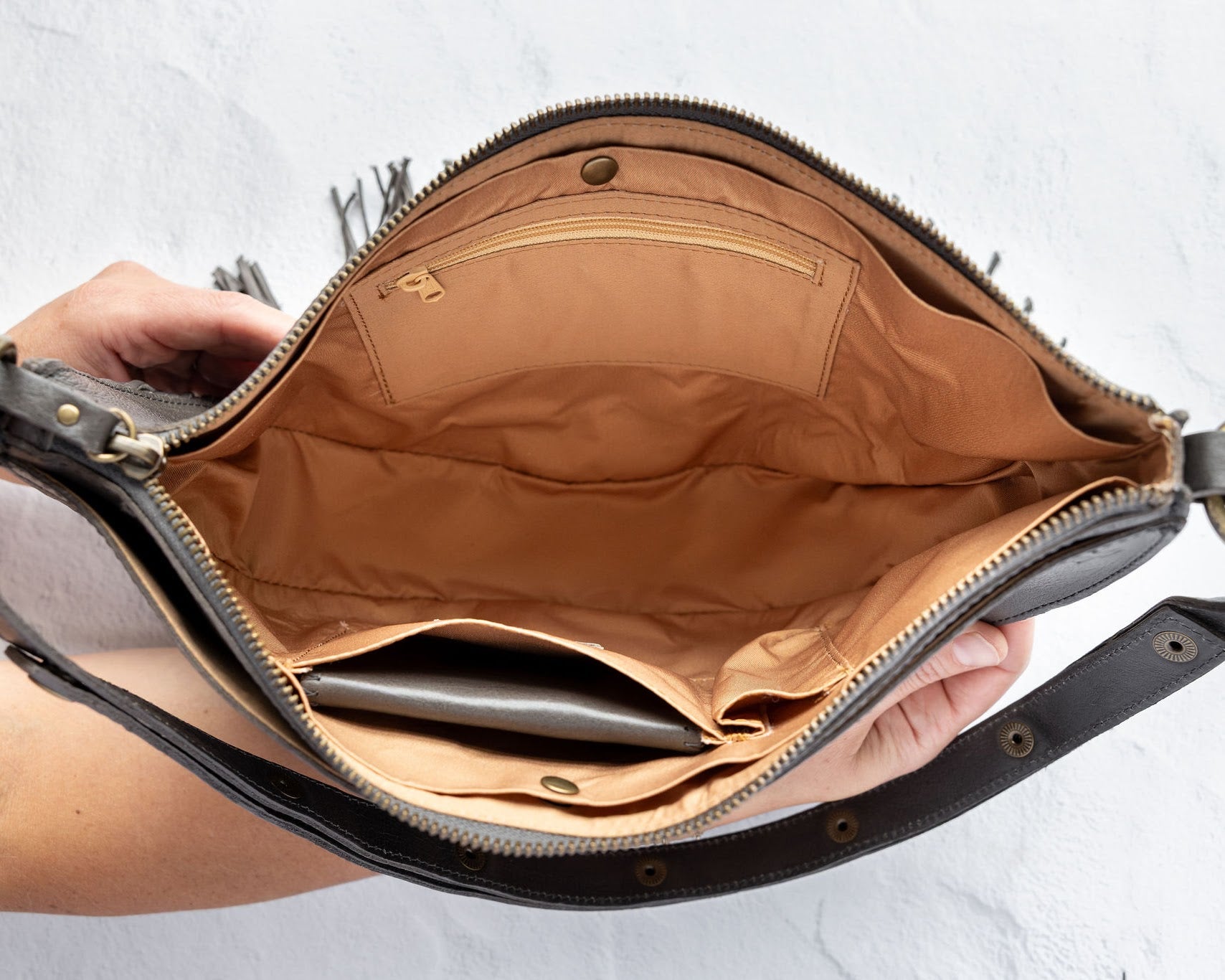 Charcoal leather fringe bag with interior pockets, held by a person against a white background