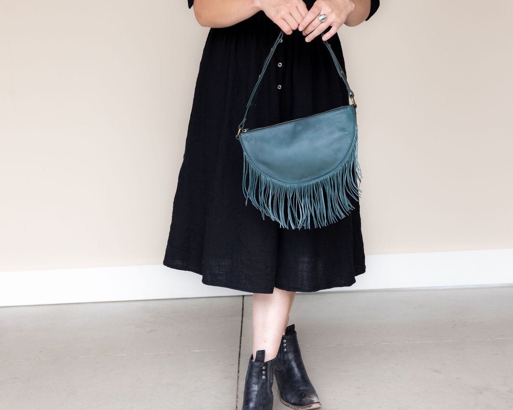 Medium teal leather fringe bag held as a clutch