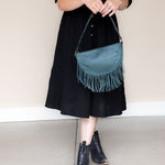 Medium teal leather fringe bag held as a clutch