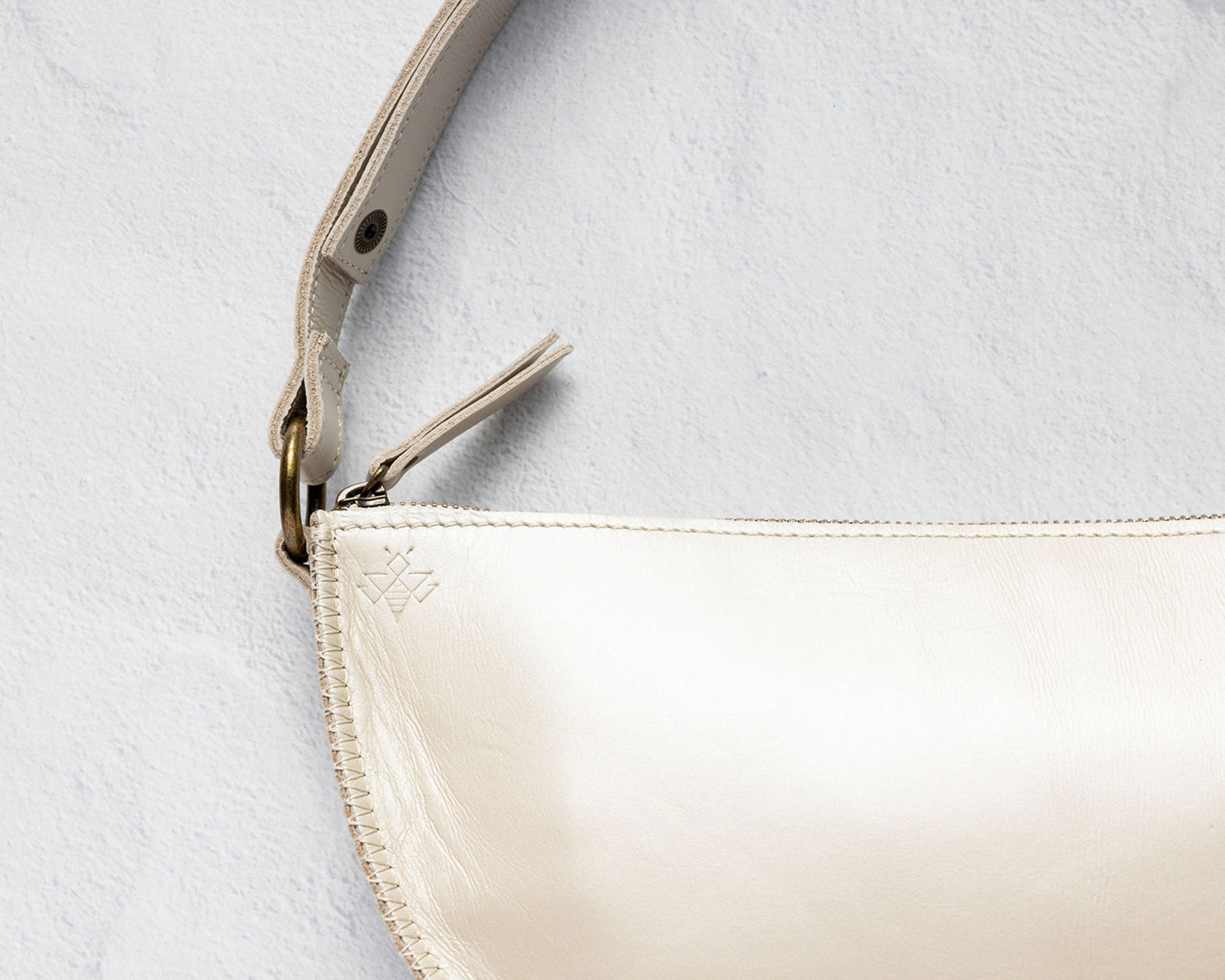 Close-up of a cream-colored leather shoulder bag with a matching leather strap and gold-tone hardware, set against a textured light gray background.