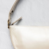 Close-up of a cream-colored leather shoulder bag with a matching leather strap and gold-tone hardware, set against a textured light gray background.