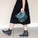 Small teal leather fringe bag held as a clutch
