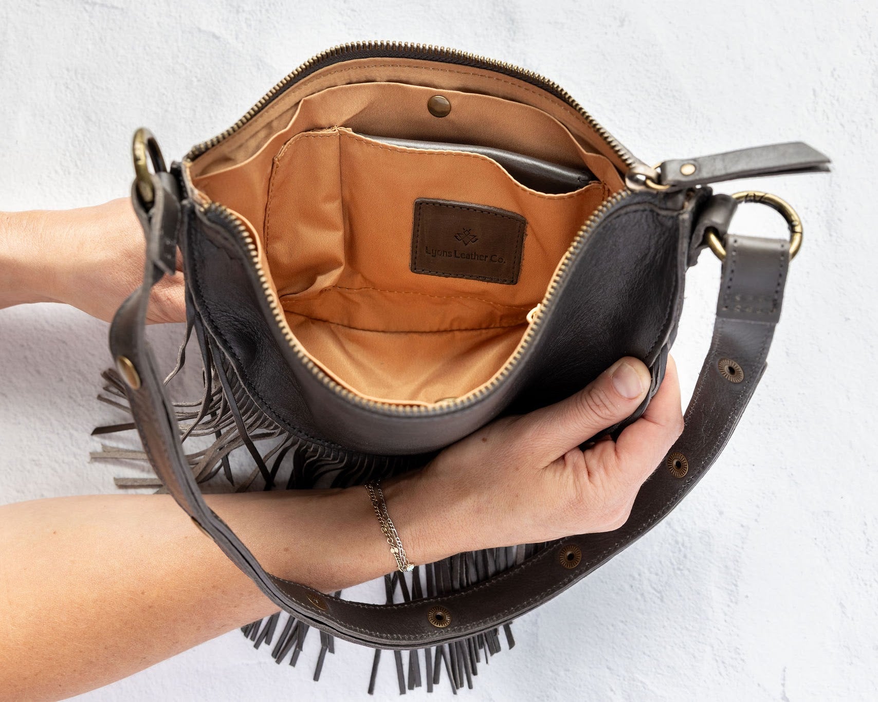 Charcoal leather fringe bag held open by a hand, showing the Gold lining, on a white background