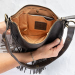 Charcoal leather fringe bag held open by a hand, showing the Gold lining, on a white background