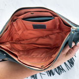 Teal leather fringe bag held open by a hand, showing the Pecan lining, on a white background