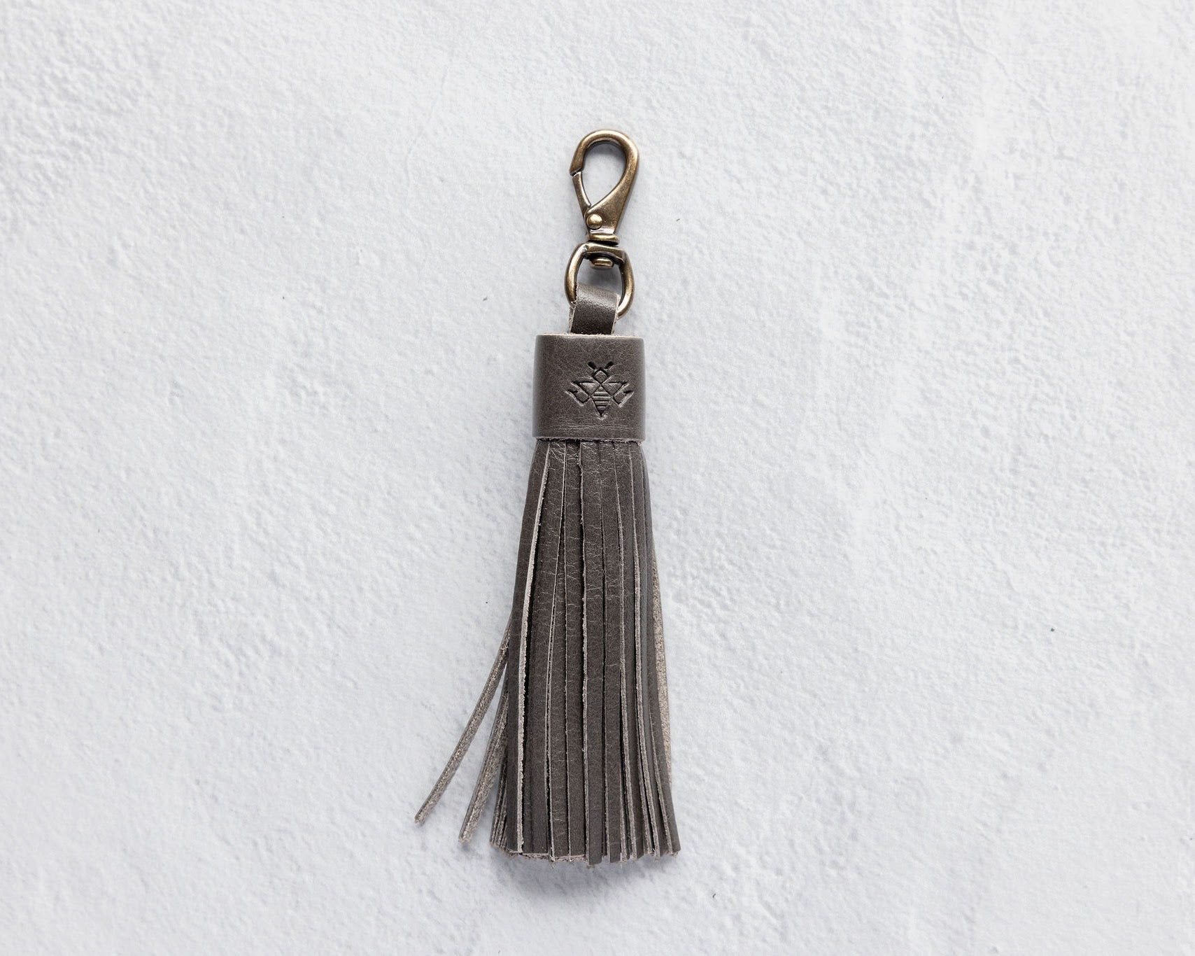 Charcoal leather tassel keychain on a white textured background