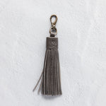Charcoal leather tassel keychain on a white textured background