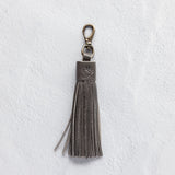 Charcoal leather tassel keychain on a white textured background