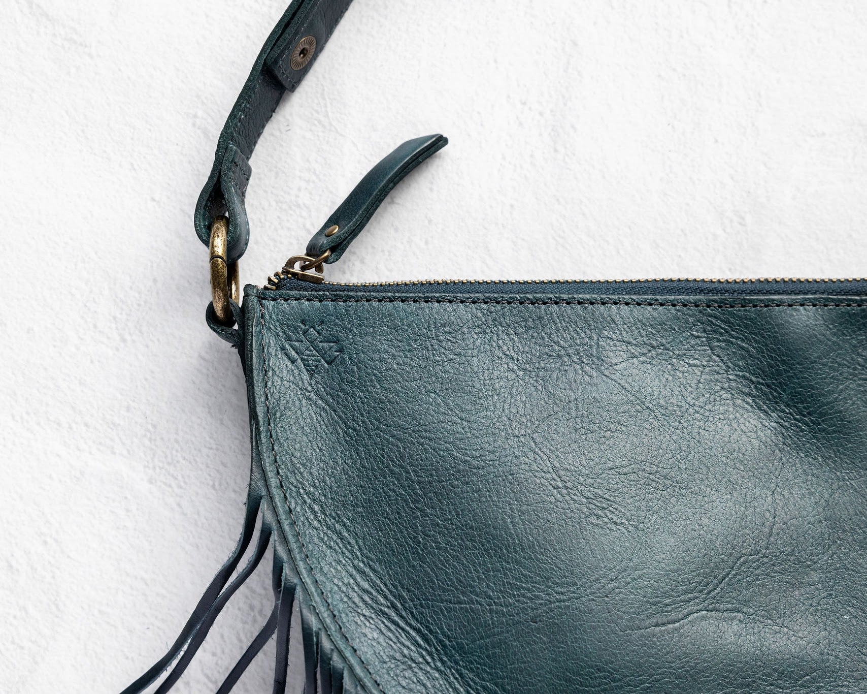 Close-up of the zipper and fringe on a teal leather bag