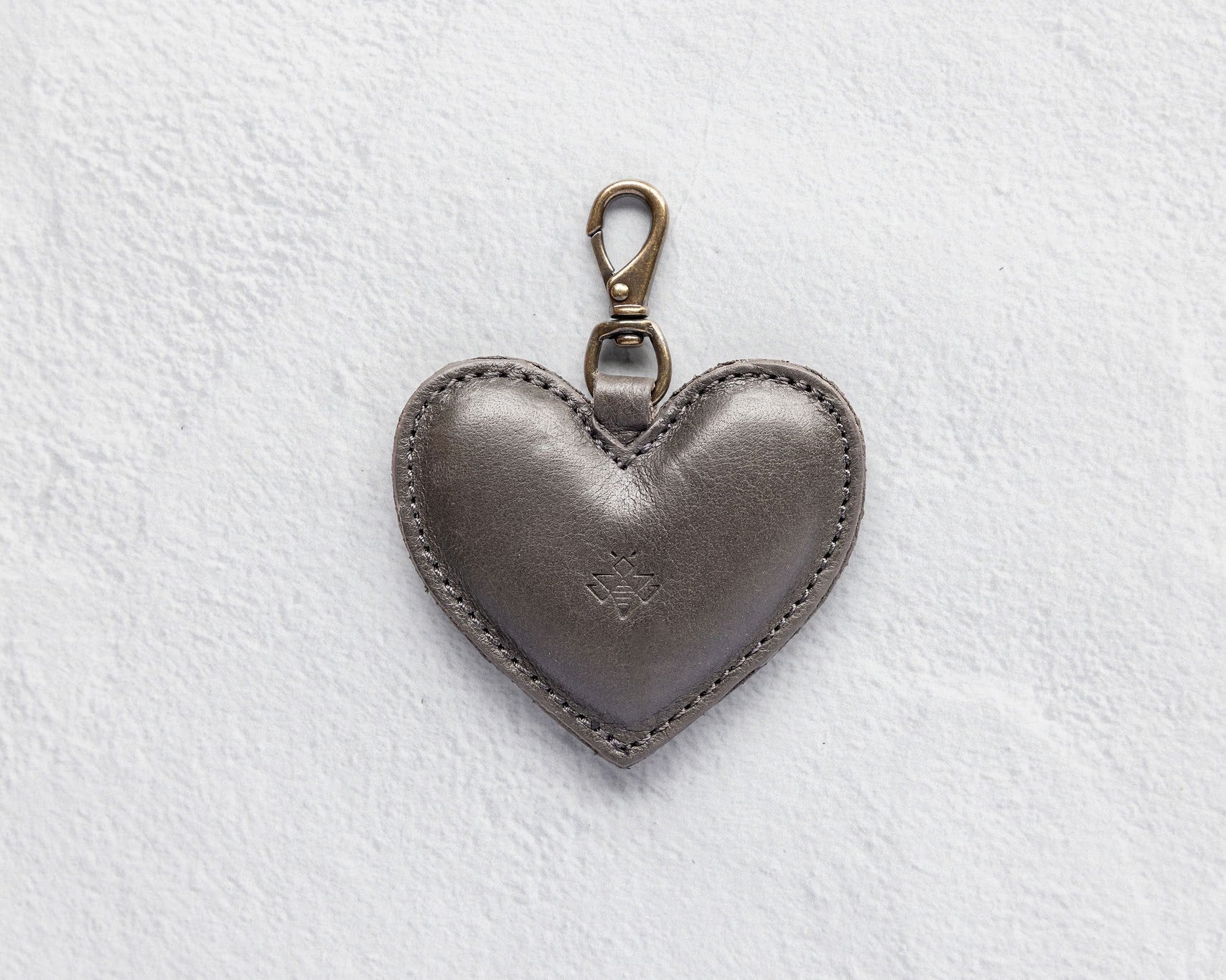 A heart-shaped charcoal leather bag charm with a brass lobster clasp