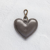A heart-shaped charcoal leather bag charm with a brass lobster clasp
