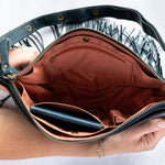 Teal leather fringe bag with interior pockets, held by a person against a white background