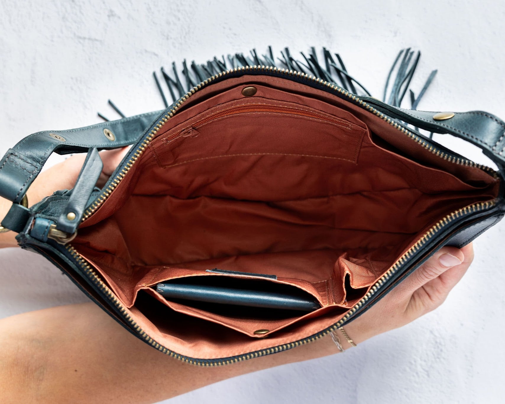 Teal leather fringe bag with interior pockets, held by a person against a white background