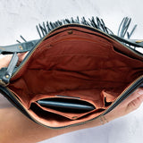 Teal leather fringe bag with interior pockets, held by a person against a white background