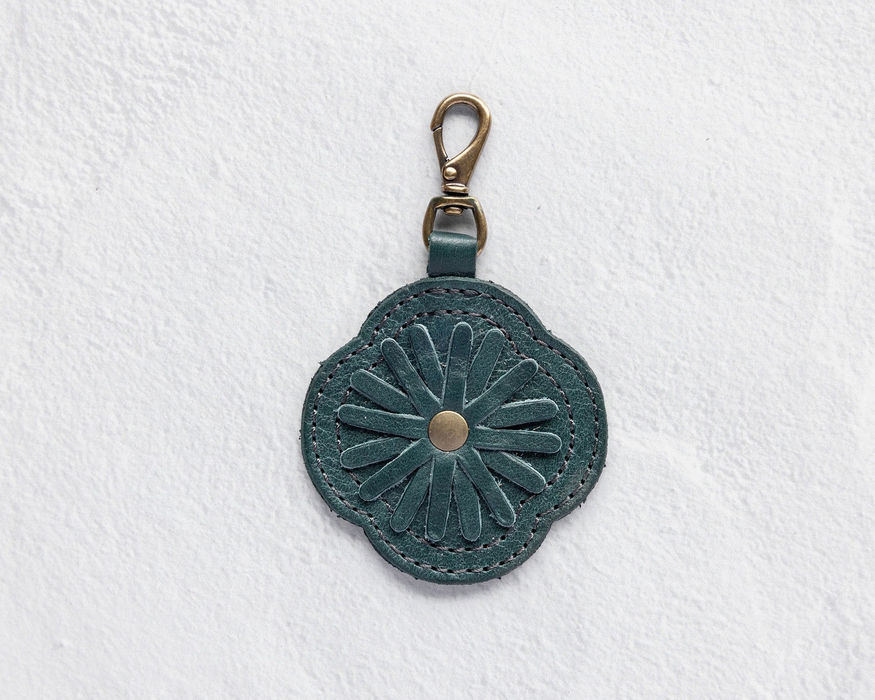 A teal leather flower-shaped bag charm with a metal lobster clasp