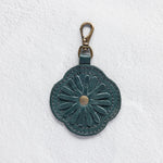 A teal leather flower-shaped bag charm with a metal lobster clasp