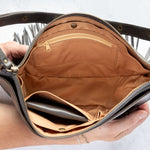 Charcoal leather fringe bag with interior pockets, held by a person against a white background