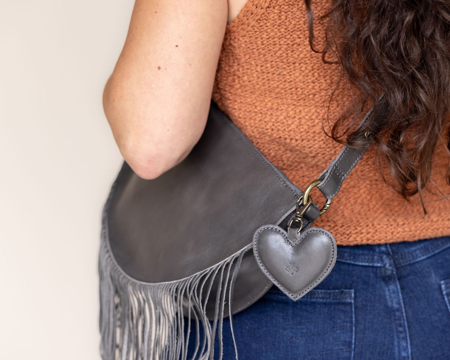 A heart-shaped charcoal leather bag charm with a brass lobster clasp