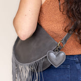 A heart-shaped charcoal leather bag charm with a brass lobster clasp
