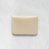 A minimalist cream-colored leather card holder or wallet with visible stitching and a debossed logo, displayed on a textured white background.