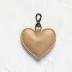 A light tan leather heart-shaped keychain with a silver metal lobster clasp, shown on a textured white background.