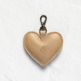 A light tan leather heart-shaped keychain with a silver metal lobster clasp, shown on a textured white background.