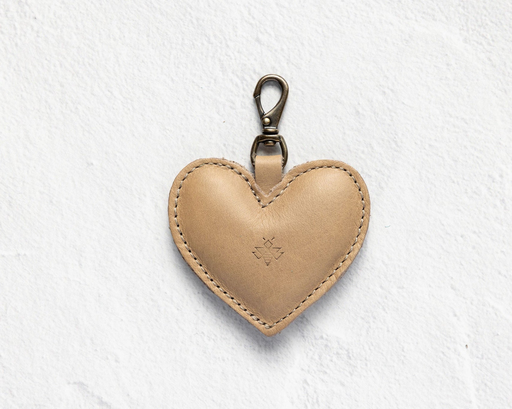 A light tan leather heart-shaped keychain with a silver metal lobster clasp, shown on a textured white background.