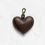 A dark brown leather heart-shaped keychain with a metal lobster clasp, shown on a textured white background.