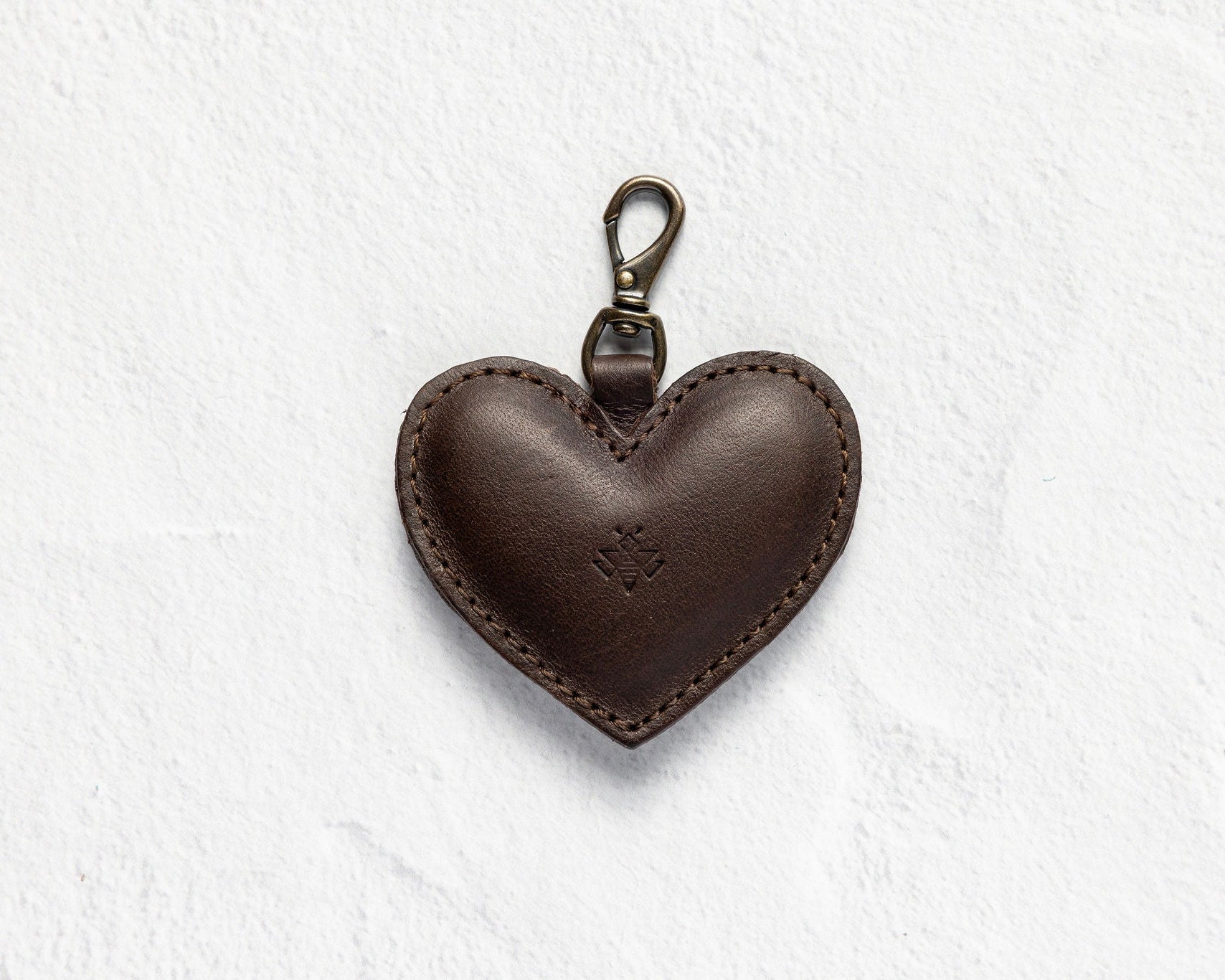 A dark brown leather heart-shaped keychain with a metal lobster clasp, shown on a textured white background.
