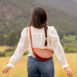 Woman wearing the Woven Terracotta & Seashell Biggie Bee crossbody in a mountain field