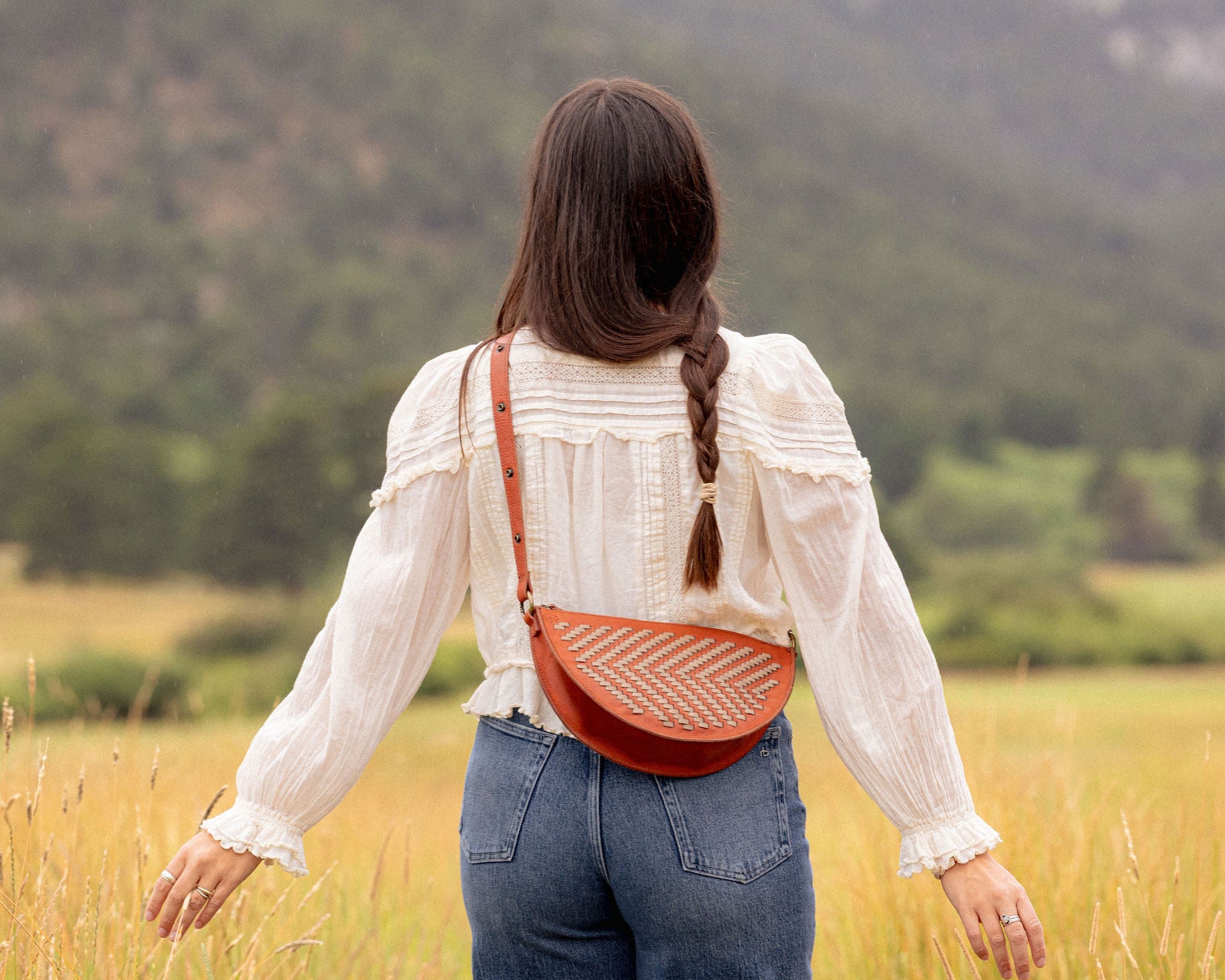 Woman wearing the Woven Terracotta & Seashell Biggie Bee crossbody in a mountain field