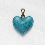 A turquoise blue textured leather heart-shaped keychain with a brass clasp, displayed on a white textured background.