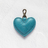 A turquoise blue textured leather heart-shaped keychain with a brass clasp, displayed on a white textured background.