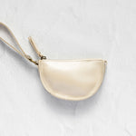 A small cream-colored leather wristlet pouch with a matching wrist strap and gold-tone zipper, displayed on a textured white background.