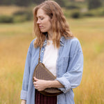 Woman wearing the Woven Sage & Espresso Biggie Bee crossbody in a mountain field