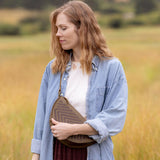 Woman wearing the Woven Sage & Espresso Biggie Bee crossbody in a mountain field