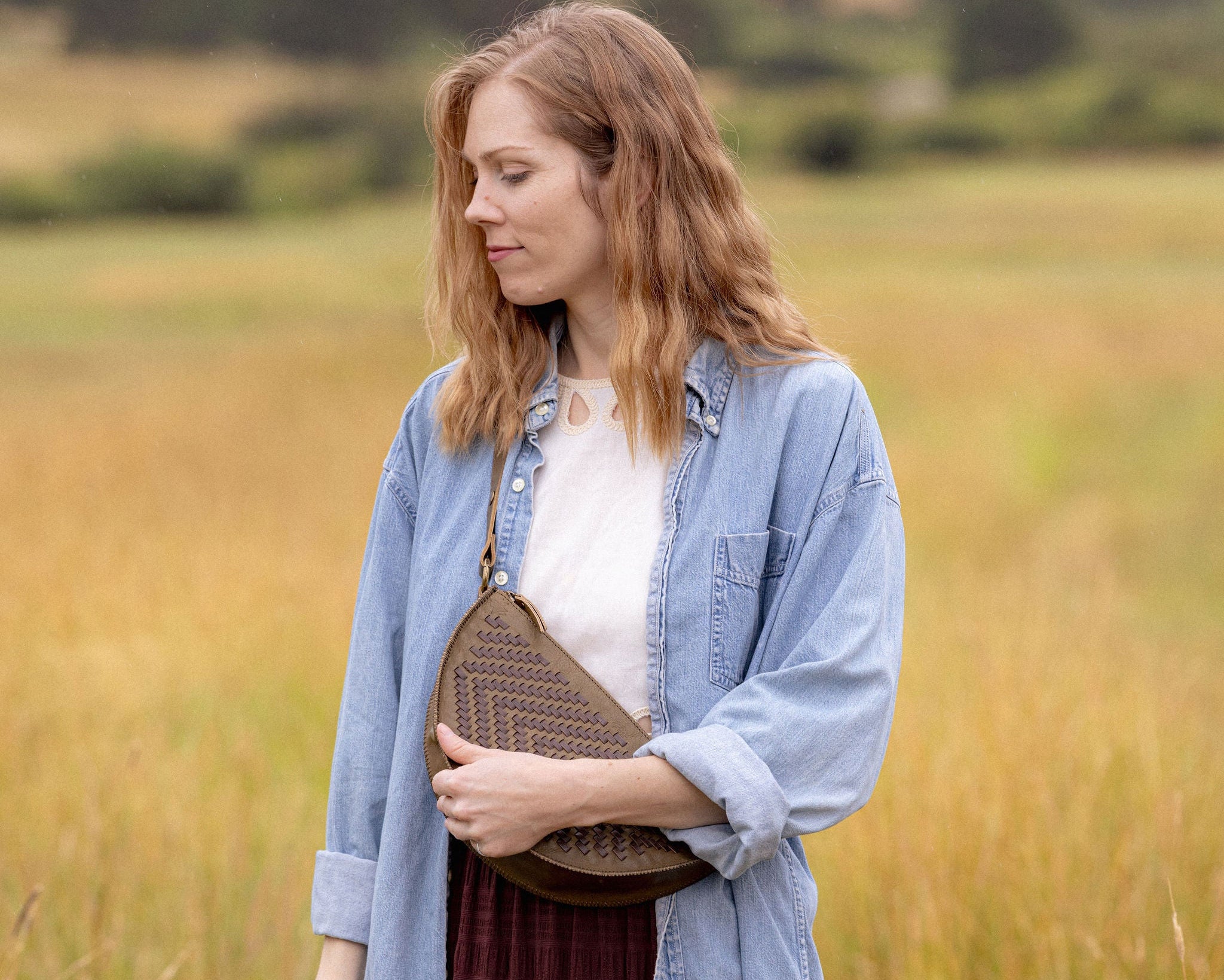 Woman wearing the Woven Sage & Espresso Biggie Bee crossbody in a mountain field