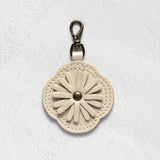 A cream-colored leather keychain or bag charm with a stitched daisy flower design and a silver-tone metal clasp, shown against a textured white background.