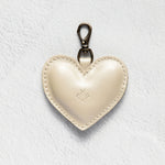 A cream-colored leather heart-shaped keychain with a silver-tone lobster clasp, displayed on a textured white background.