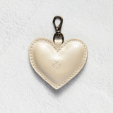 A cream-colored leather heart-shaped keychain with a silver-tone lobster clasp, displayed on a textured white background.