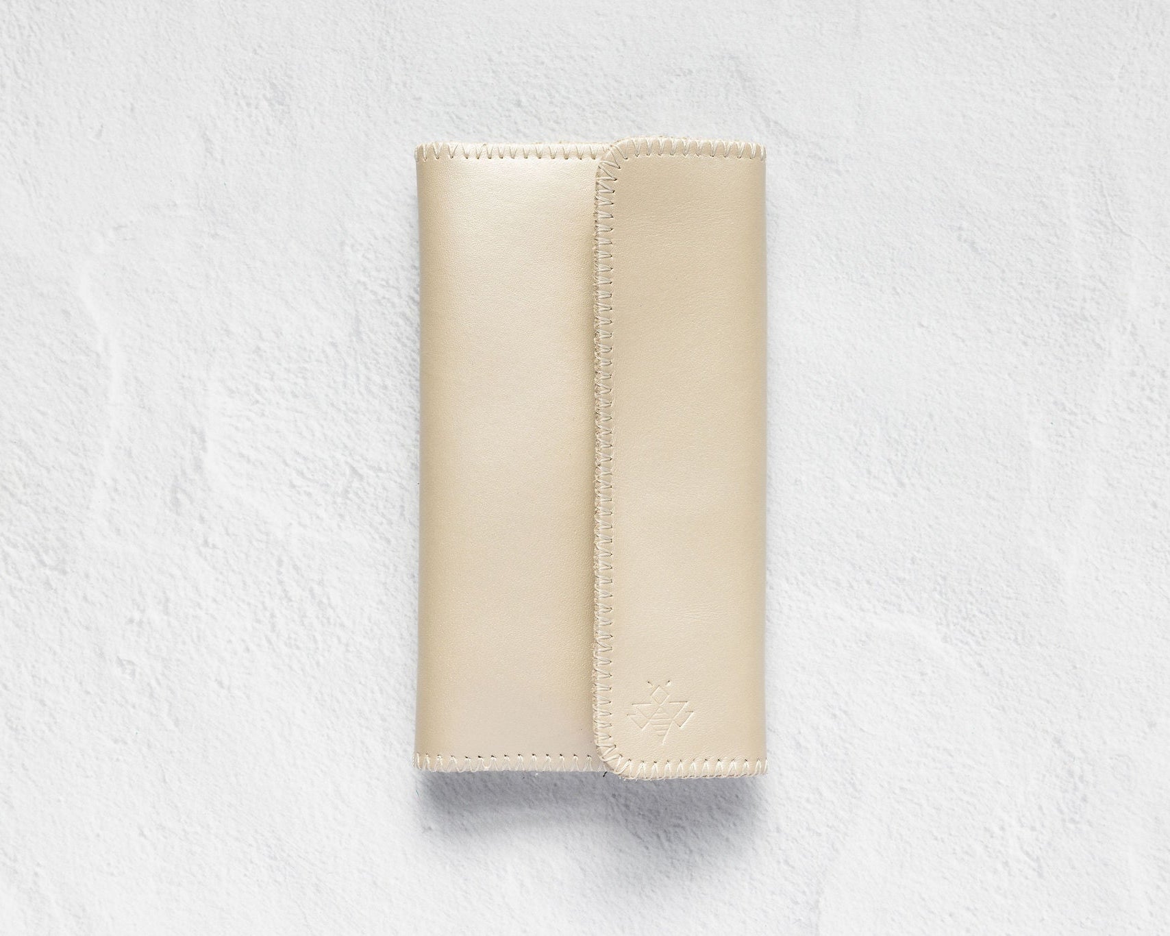 A light beige leather wallet or card holder with a vertical stitched fold, shown flat against a textured white background.