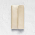 A light beige leather wallet or card holder with a vertical stitched fold, shown flat against a textured white background.